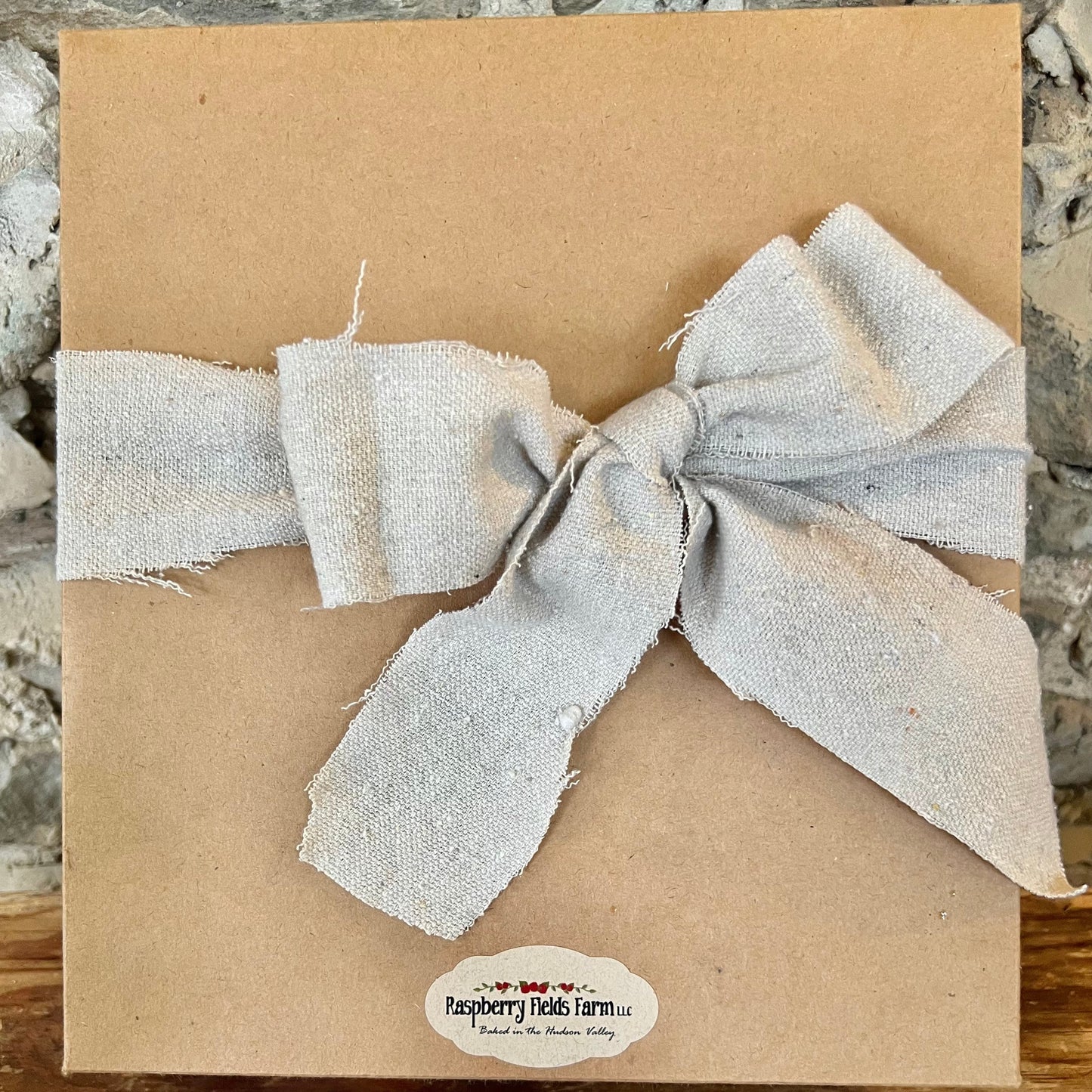 Brown paper package with a textured beige bow on a stone surface