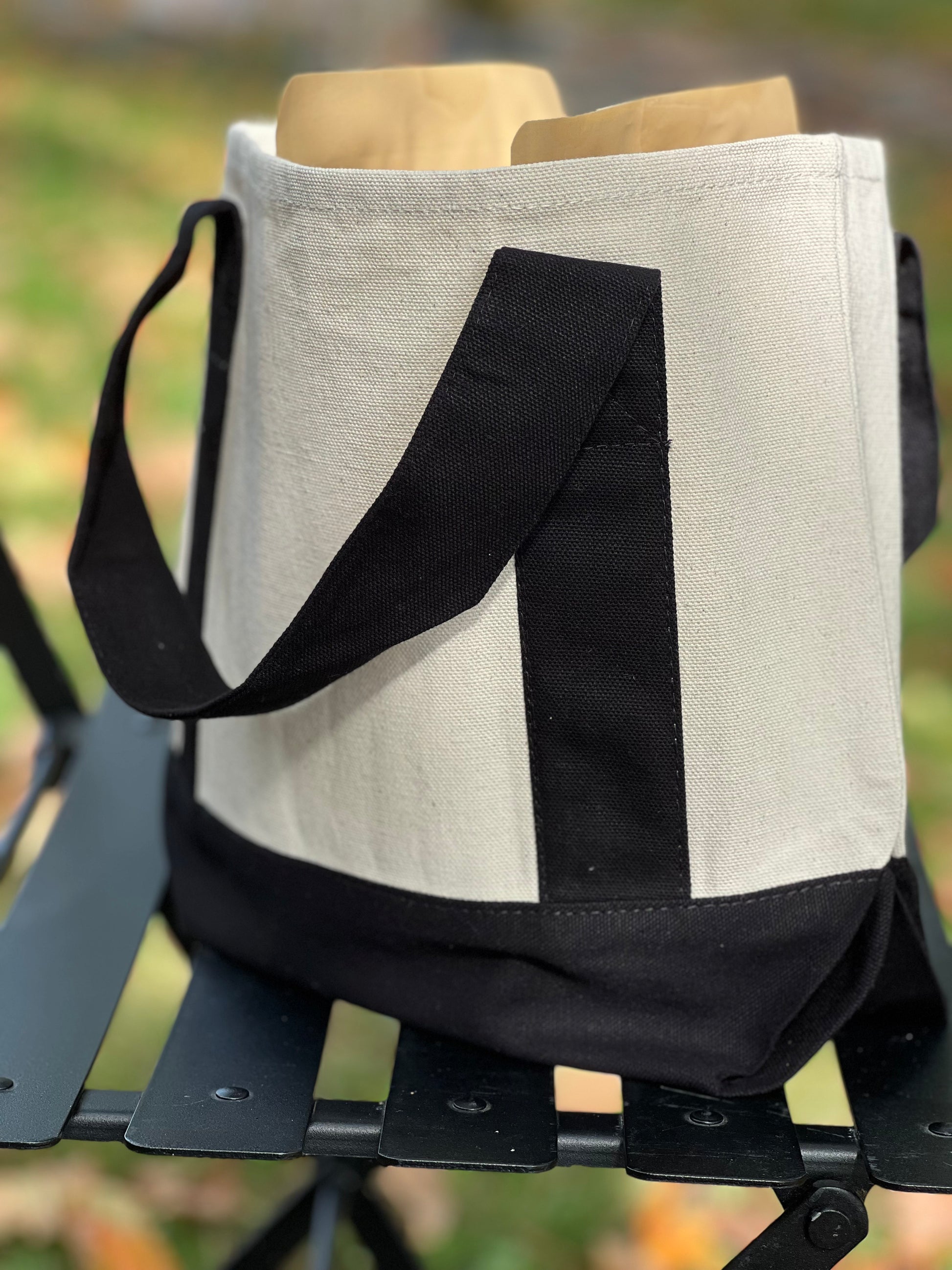 Beige tote bag with black strap on a metal stand outdoors