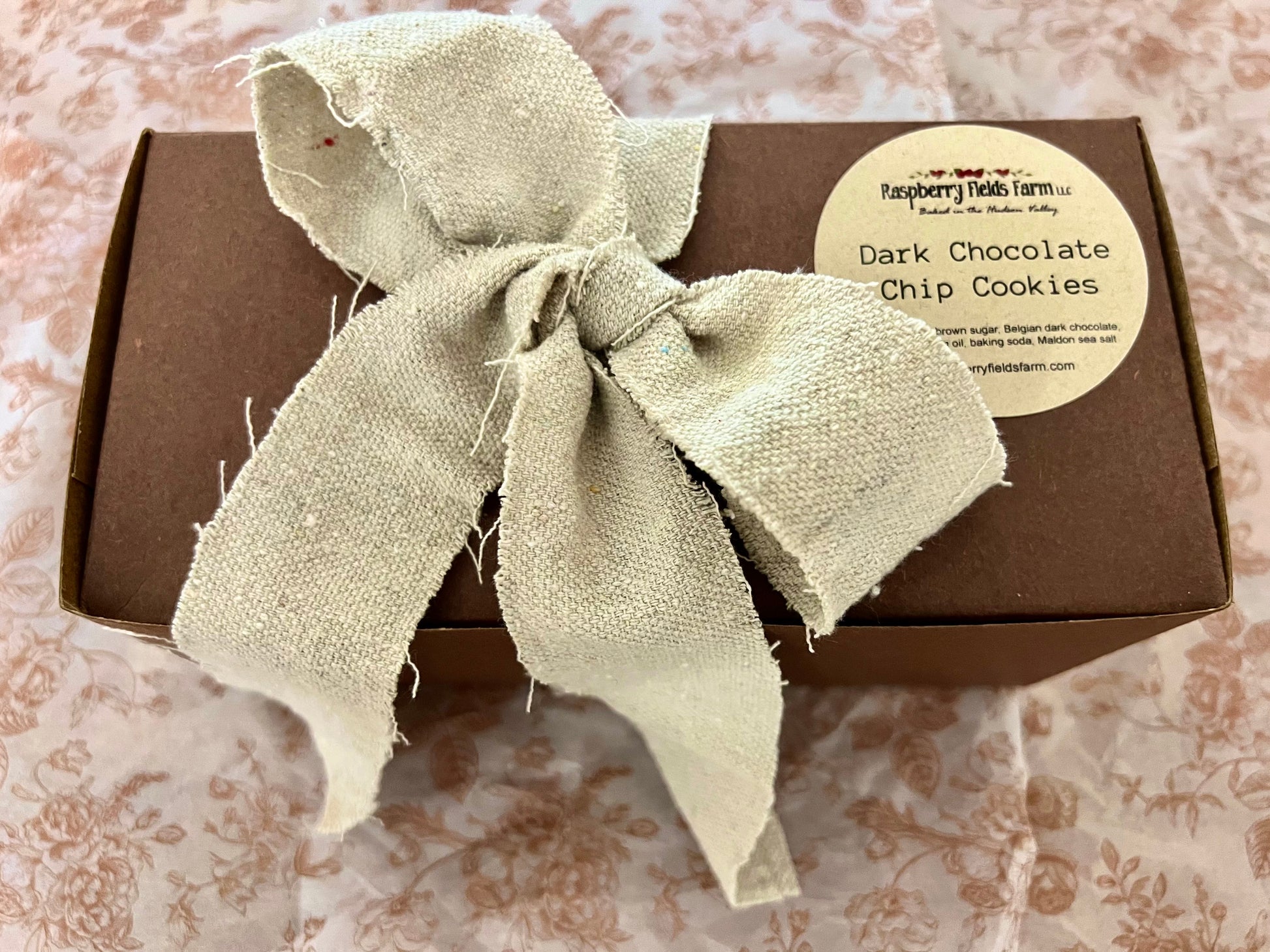 Box of dark chocolate chip cookies with a tan ribbon on a patterned surface