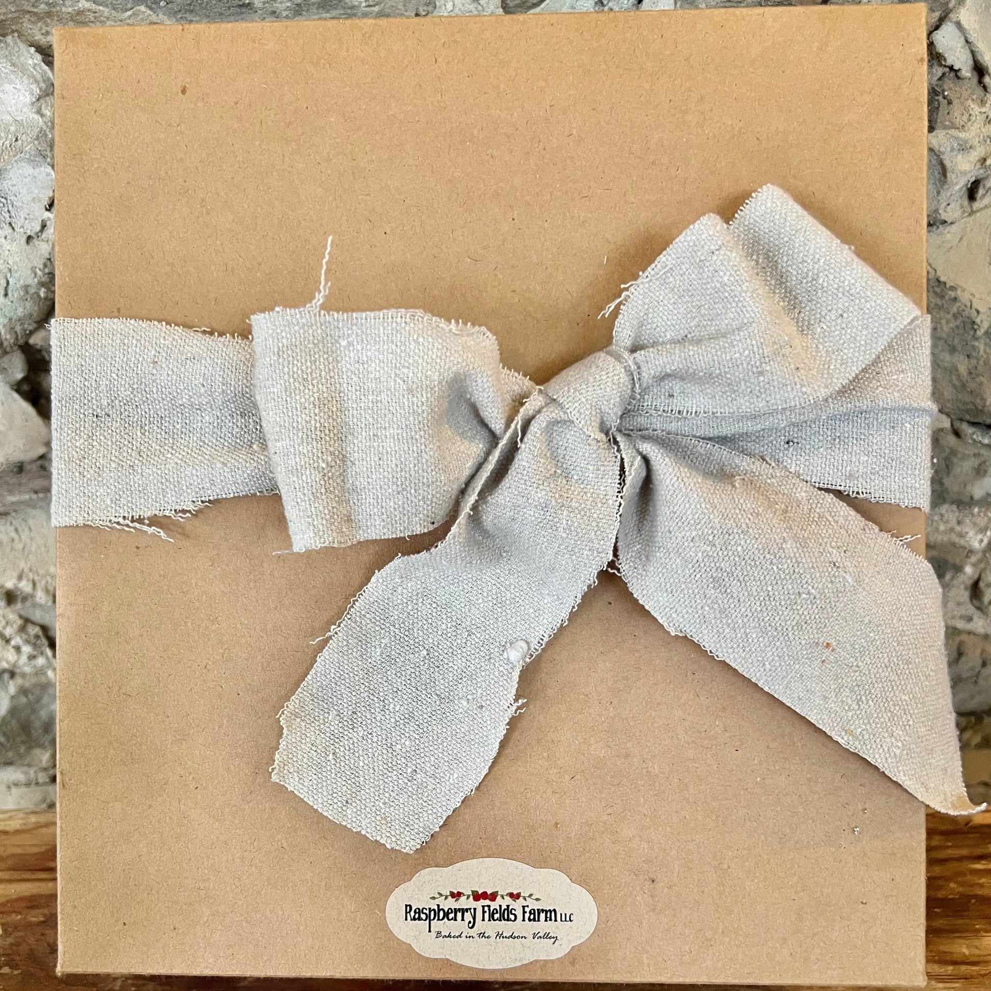 Brown paper package with a textured beige bow on a stone surface